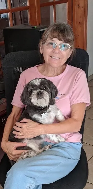 Betty smiling while holding a shih tzu on her lap at home