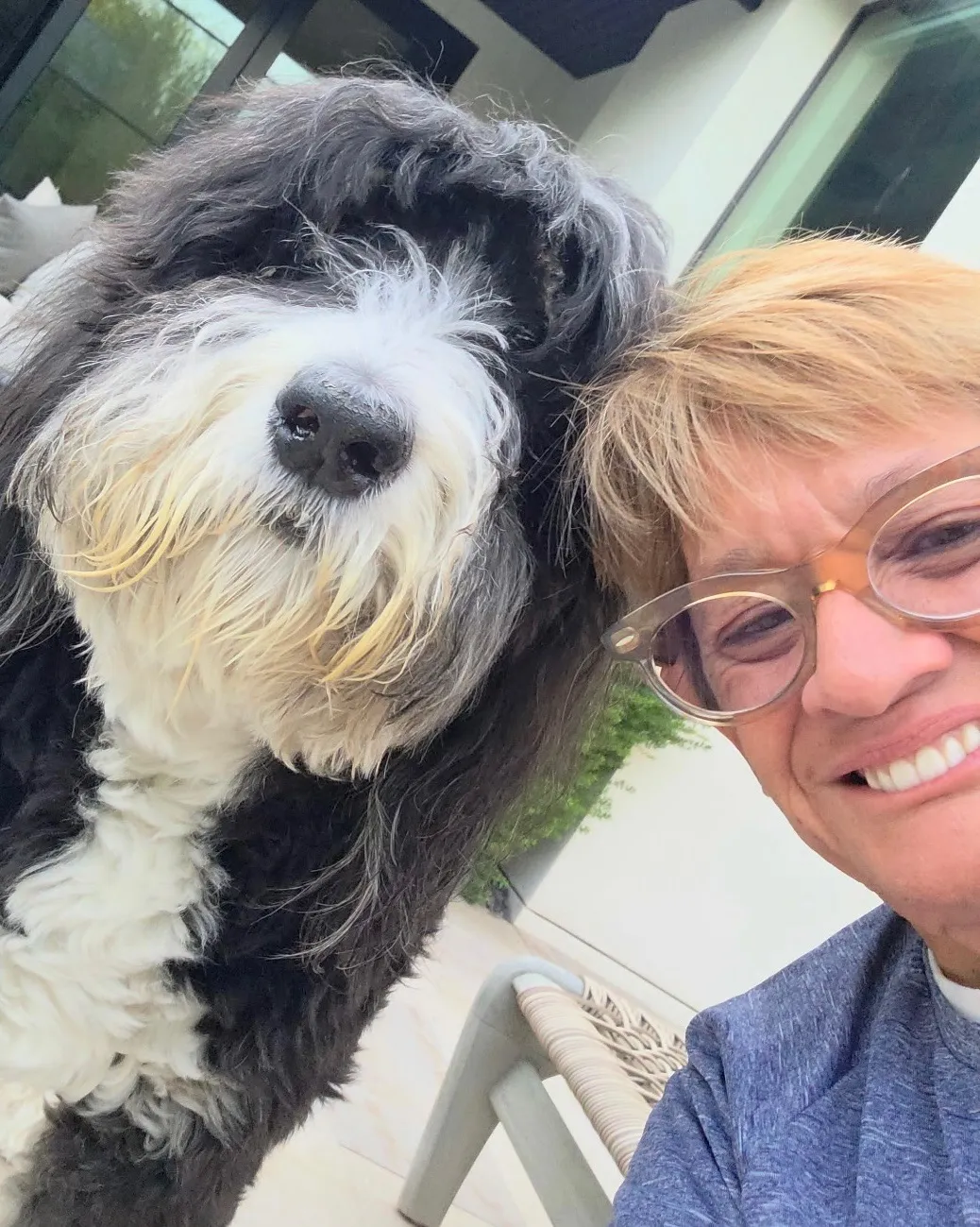 Marty smiling next to a shaggy black and white sheepadoodle leaning its head against her